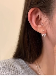 Close-up of elegant silver bow earrings with zircon on a model wearing a grey sweater