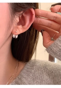 Close-up of elegant cubic zirconia bow earrings worn on ear with sparkling silver details