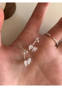 Macro detail of silver bow earrings with zircon stones held in palm for size reference
