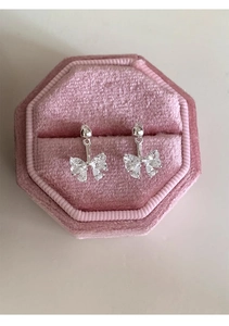 Macro view of silver bow-shaped zircon earrings nestled in a pink velvet jewelry box