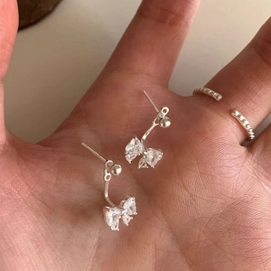 Elegant silver bow stud earrings featuring sparkling zircon crystals held in palm for scale