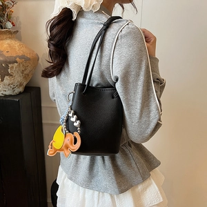 Detail der schwarzen Beuteltasche aus genarbtem Leder mit buntem Elefantenanhänger am Model