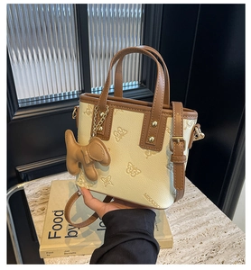 Detail of beige bucket bag with embossed butterfly pattern and brown puppy charm