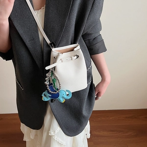 Detail der weißen Mini-Eimertasche aus Narbenleder mit Elefantenanhänger am Modell