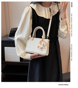 Détail du mini sac seau blanc texturé avec charm cheval rose et poignée tressée sur modèle