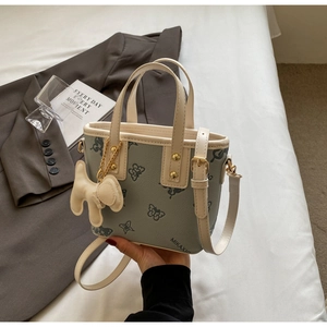 Detail of green butterfly embossed bucket bag with puppy charm on white bedding