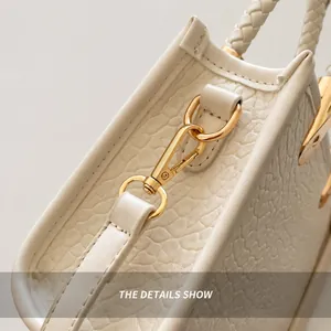 Gros plan sur les crochets dorés et la poignée tressée du sac en cuir texturé beige