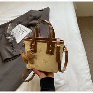 Close-up of butterfly embossed cream bucket bag with brown trim and cute puppy charm