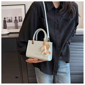 Détail d'un sac seau bleu clair avec poignée tressée et charm cheval sur un mannequin