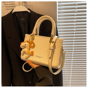 Détail d'un mini sac cabas beige avec poignées tressées et accessoire charm de cheval