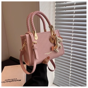 Détail d'un sac seau en cuir rose texturé avec poignée tressée et breloque petit cheval