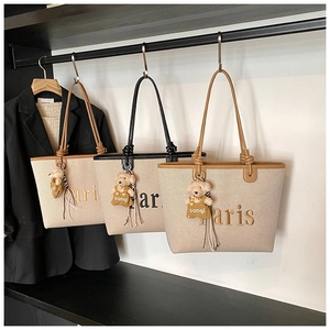 Detail view of canvas tote bags with Paris embroidery and plush bear charms hanging on a rack