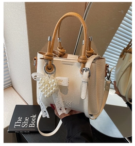 Detail of white embossed leather bag with heart pearl charm and brown handle