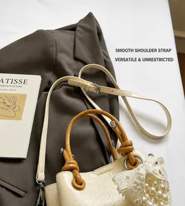Detail of detachable strap and pearl lace ornament on creamy white bucket bag