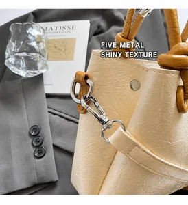 Detail of cream bucket bag with glossy pleated leather and brown knotted handle strap