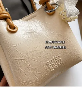 Detailed macro view of off-white pleated leather bag with brown knotted handle and lace pendant