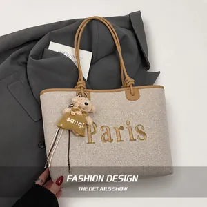 Detail of beige canvas tote with Paris embroidery and cute bear charm on a suit background