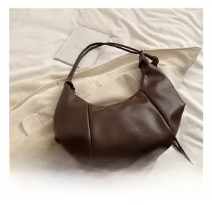 Close-up of dark brown half-moon bag featuring unique knotted strap and pleated leather texture