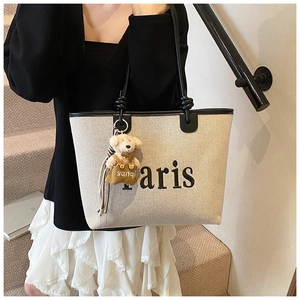 Close-up of canvas bucket bag with black leather straps and a cute teddy bear charm