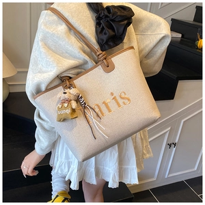 Detail of beige canvas tote with brown leather trim and Paris embroidery with bear charm