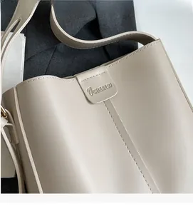 Gros plan d'un sac seau en cuir beige avec coutures fines et logo de marque en relief