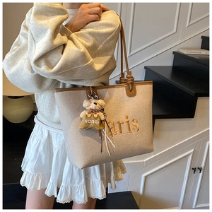 Detail of beige canvas tote bag with brown leather trim, Paris embroidery, and teddy bear charm
