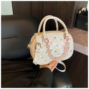 Detail of cream quilted mini Boston bag featuring pink beaded bow charm and silver studs