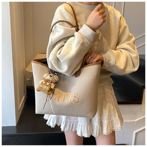 Detail of canvas bucket bag with Paris embroidery and plush bear charm for daily use