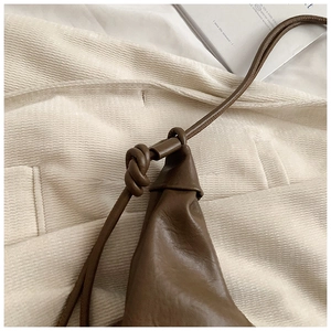Macro shot of brown leather texture and unique knotted shoulder strap detail on a hobo bag