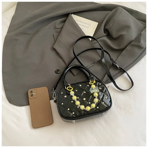 Detail of black quilted patent leather Boston bag with decorative bead chain and metal feet