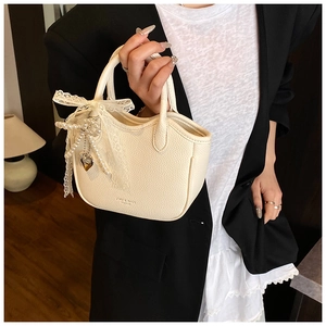 Close-up of cream lychee texture handbag featuring lace bow and pearl heart charm detail