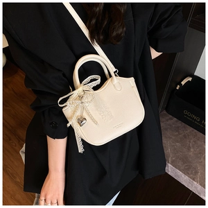 Close-up of white leather handbag featuring delicate lace bow and pearl heart charm details