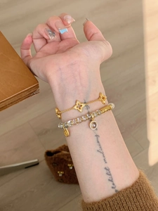 Detail of layered gold clover chain and transparent beaded bracelet set on wrist