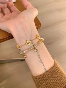 Detail of white crystal bead bracelet layered with gold clover charms on a knitted sleeve