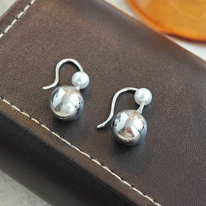 Elegant silver teardrop earrings with white pearls displayed on premium brown leather
