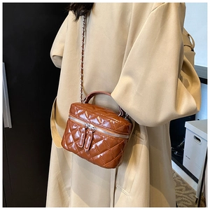 Detail of a brown quilted bucket bag with shiny patent finish and silver chain strap