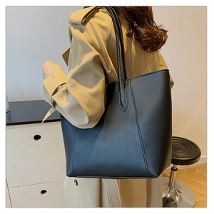 Détail d'un grand sac cabas noir en similicuir porté par un mannequin avec un trench