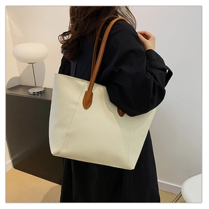 Detail view of large tote bag with brown straps and vertical stitching on beige leather