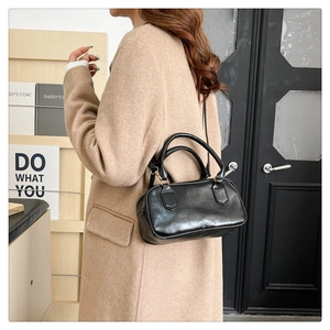 Sac bowling noir avec ferrures dorées porté sur un élégant manteau en laine beige