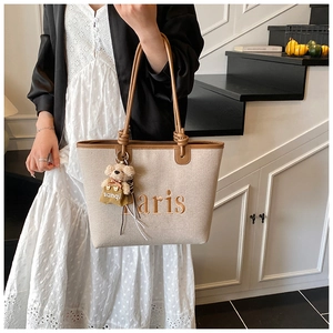 Detail of canvas tote bag with Paris embroidery, leather handles, and a teddy bear charm