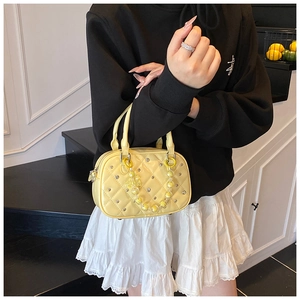 Detail of yellow quilted patent leather mini bag with silver studs and pearl chain