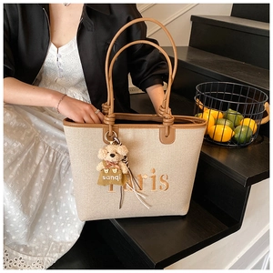 Detail of beige canvas tote with brown leather trim and cute plush bear accessory