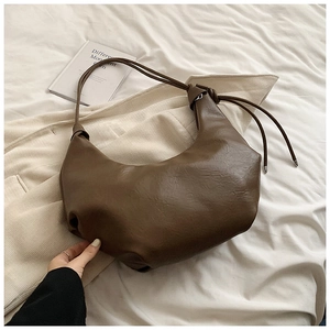 Detail of a brown leather crescent moon bag with knot strap on soft white fabric