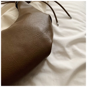 Close-up of brown soft leather bag featuring vintage pleated texture and metal tipped drawstring