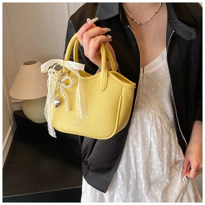 Detail of yellow lychee leather handbag with lace bow and pearl heart charm accessory