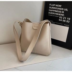 Détail d'un sac seau crème montrant la bandoulière large et le logo embossé sur le cuir