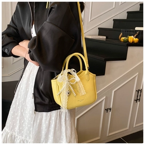 Close-up of yellow pebble leather handbag with lace bow charm and pearl detail