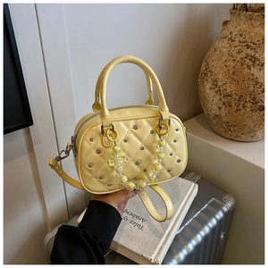 Detail of yellow quilted Boston bag with studs and bead chain on a suitcase