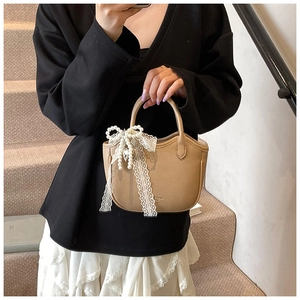 Elegant khaki leather handbag with pearl and lace bow pendant held by model on stairs
