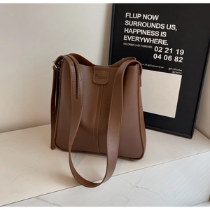 Détail de sac seau en cuir marron avec logo embossé sur surface en marbre blanc